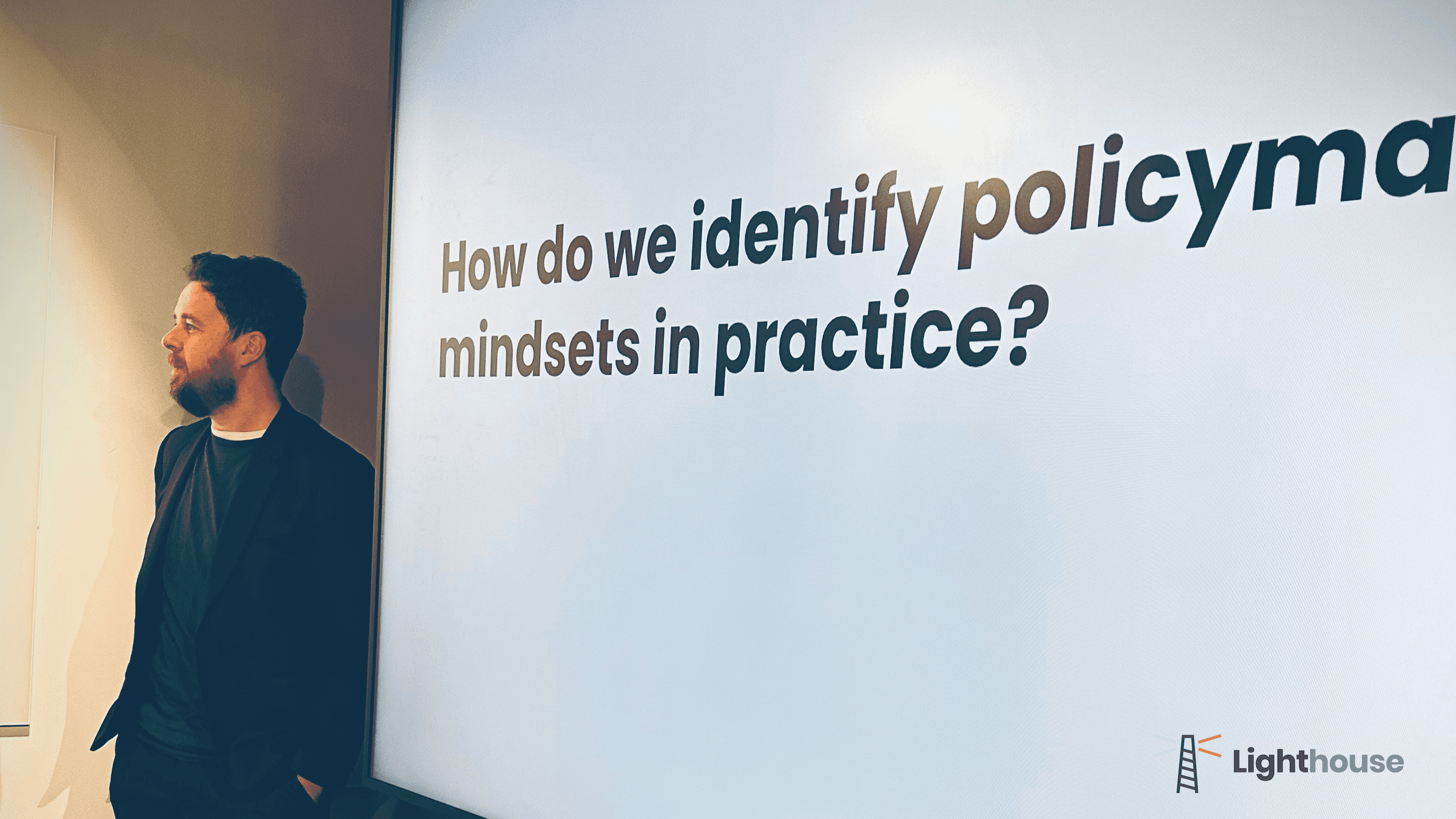 A Lighthouse session in progress: a presenter standing beside a projected slide reading “How do we identify policymaker mindsets in practice?”